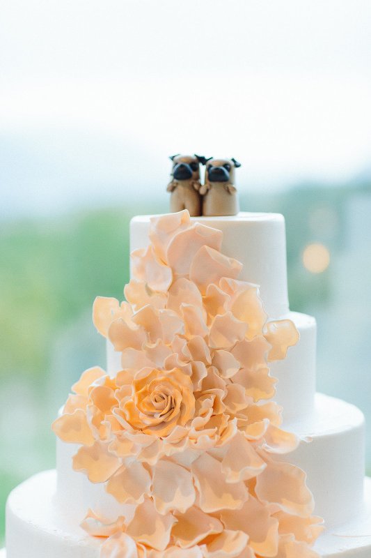 A white wedding cake decorated with a large orange sugar bloom and topped with two little dog cake toppers for a dog lover wedding