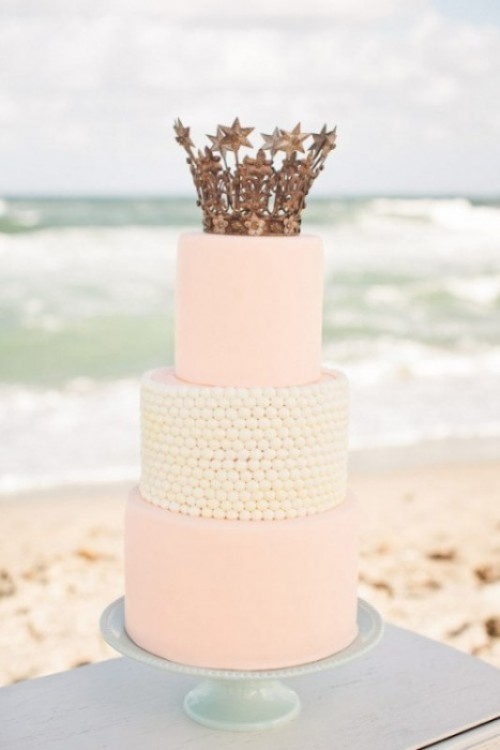 a light pink and white three-tier wedding cake topped with a crown cake topper is a great fit for a royal wedding