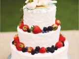 a white buttercream wedding cake decorated with fresh berries and topper with weird animal cake toppers for a touch of fun and personalization