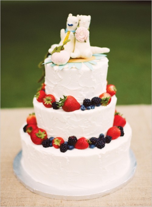 a white buttercream wedding cake decorated with fresh berries and topper with weird animal cake toppers for a touch of fun and personalization