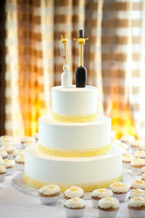 a white round wedding cake with yellow ribbons, giraffe cake toppers dressed like a couple is a fun and cute solution