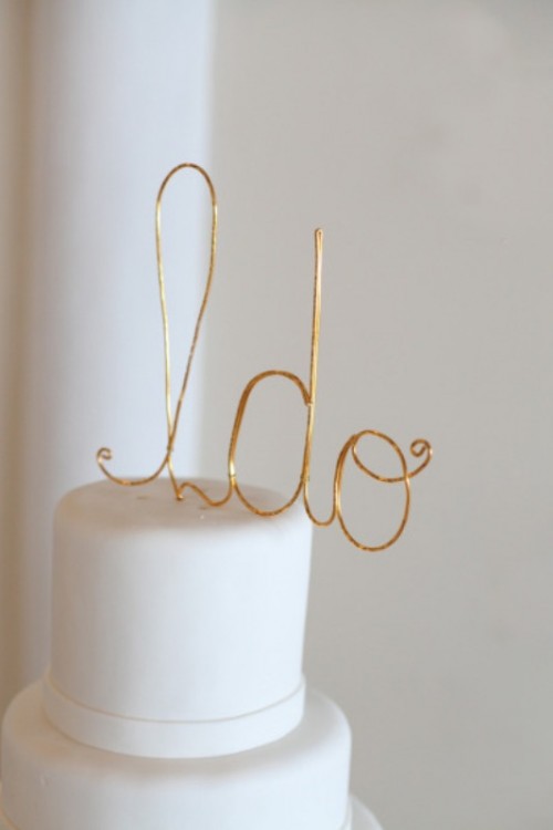 a white buttercream wedding cake with a gold calligraphy I DO cake topper is a lovely modern idea to try