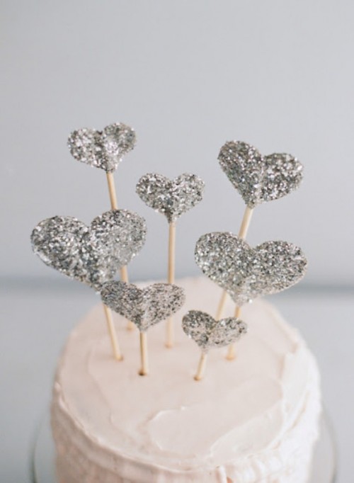 a white buttercream wedding cake topped with multiple silver glitter hearts is a gorgeous idea for a modern or glam wedding, it's an easy way to spruce up a simple cake
