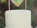 a white buttercream wedding cake with a unique cake topper – a pink heart hanging on sticks and decorated with colorful buttons is a lovely idea