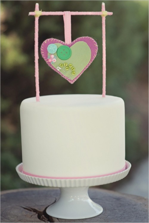 a white buttercream wedding cake with a unique cake topper - a pink heart hanging on sticks and decorated with colorful buttons is a lovely idea