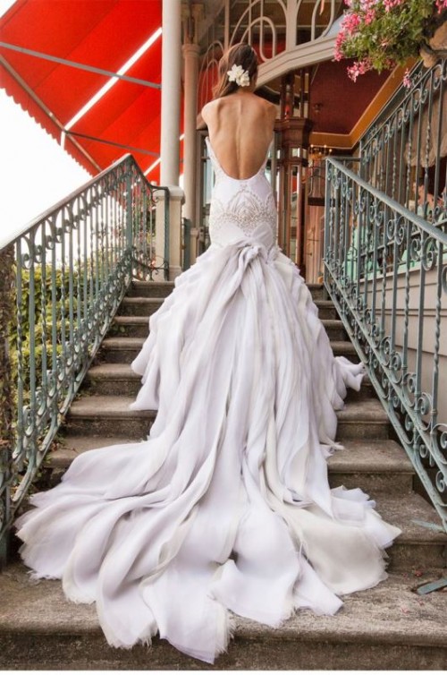 a white mermaid wedding dress with embellishments, a low back, a layered skirt with a long train is a super chic idea