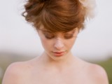 a messy wavy updo with bangs and a large faux flower for a modern bride with a touch of romance