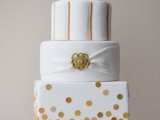 a white wedding cake with polka dot, striped and plain tiers, a white ribbon and a gold brooch is a chic and refined idea