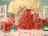 a frosted glass vase with white hydrangeas, corals, blue candle holders for a beach inspired wedding