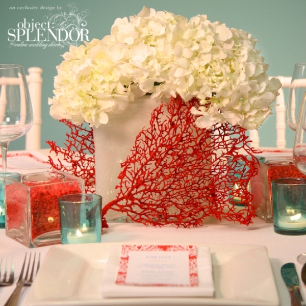A frosted glass vase with white hydrangeas, corals, blue candle holders for a beach inspired wedding