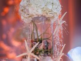 a cute beach wedding centerpiece with a jar filled with air plants and seashells, starfish and white hydrangeas on top