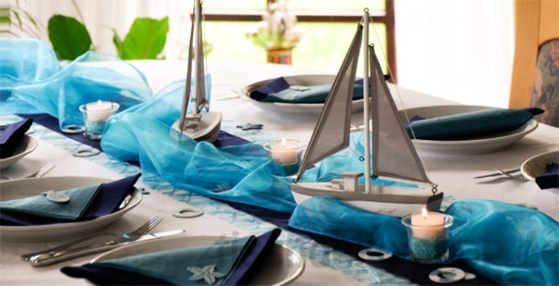 A blue table runner and boats plus candles for a beach or coastal wedding centerpiece