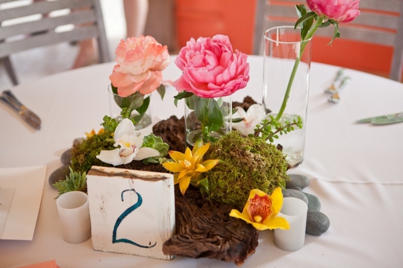 A tropical beach wedding centerpiece with driftwood, tropical blooms, a table number and candles