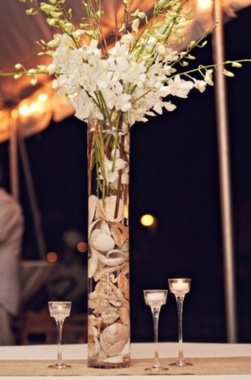 a clear vase with seashells and white blooms plus candles around for an elegant beach wedding