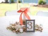 a beach wedding centerpiece with seashells, candles and a large candle holder with a ribbon bow