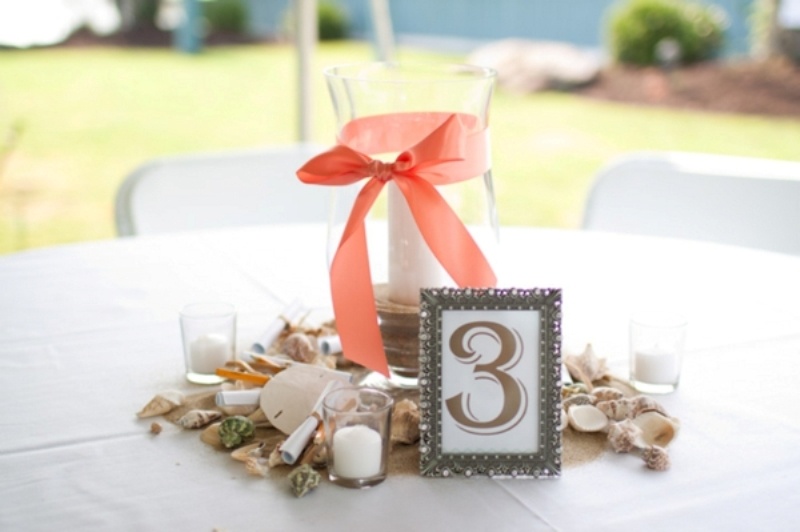 A beach wedding centerpiece with seashells, candles and a large candle holder with a ribbon bow