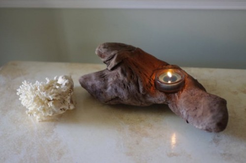 a piece of driftwood with a candle and corals is a relaxed idea of a beach wedding centerpiece
