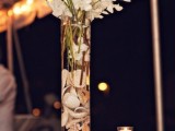 a tall clear glass vase with seashells, white blooms and candles all around