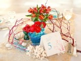 a beach wedding centerpiece with corals, seashells, branches and bright blooms in blue vases