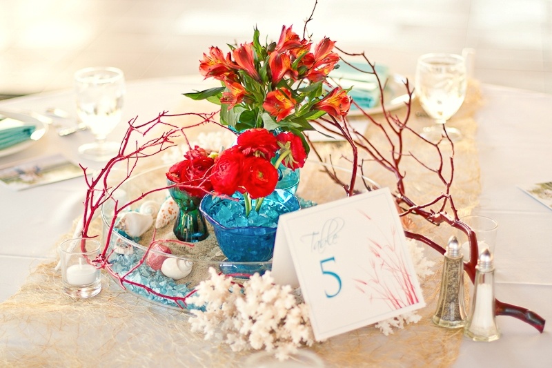A beach wedding centerpiece with corals, seashells, branches and bright blooms in blue vases