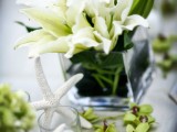 a clear vase with white lilies, green orchids and a starfish for a cute beachy wedding centerpiece