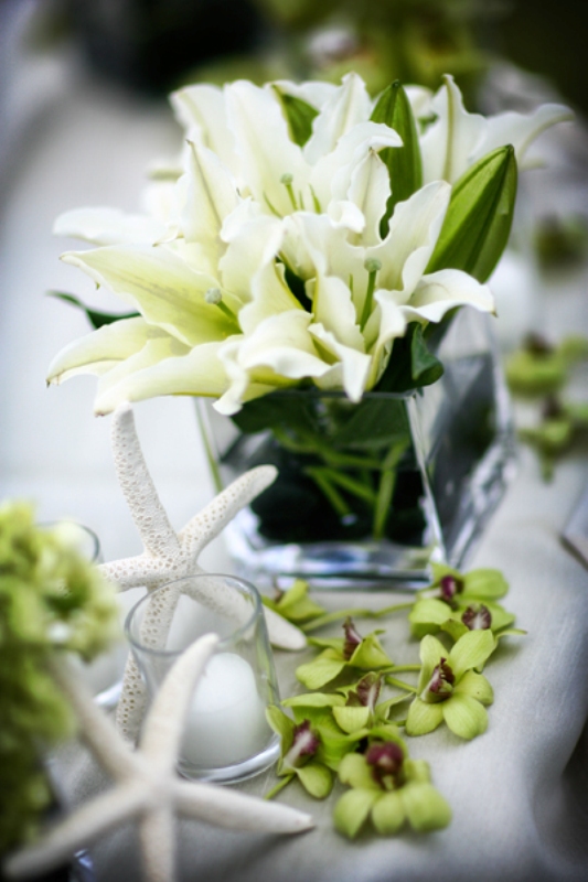 A clear vase with white lilies, green orchids and a starfish for a cute beachy wedding centerpiece