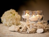 a beachy centerpiece with seashells, starfish and floating candles in clear glasses