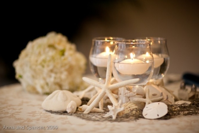 A beachy centerpiece with seashells, starfish and floating candles in clear glasses