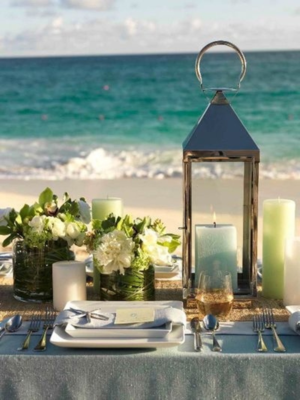 A candle lantern, green and blue candles, green and white floral arrangements in wrapped vases