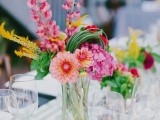 a clear vase with bright and colorful blooms plus greenery is a very fun idea for a tropical wedding