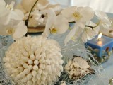 a beach wedding centerpiece of a seashell ball, seashells, candles and white orchids