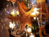 a tropical beach wedding centerpiece with a mirror, a starfish, candles and peachy callas