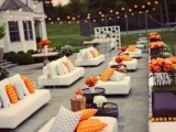 a modern outdoor wedding lounge with modern white sofas, colorful pillows, low ottomans and bright blooms