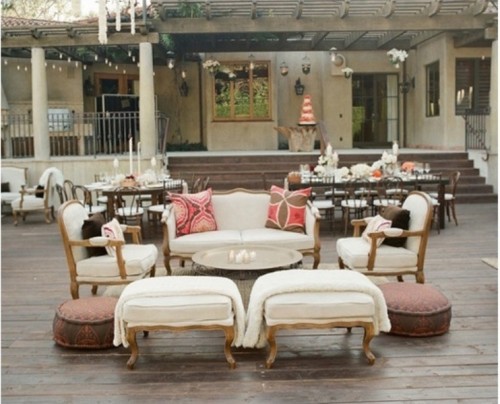 a refined vintage outdoor wedding lounge with white upholstery and bright pillows, low poufs and a round metal table
