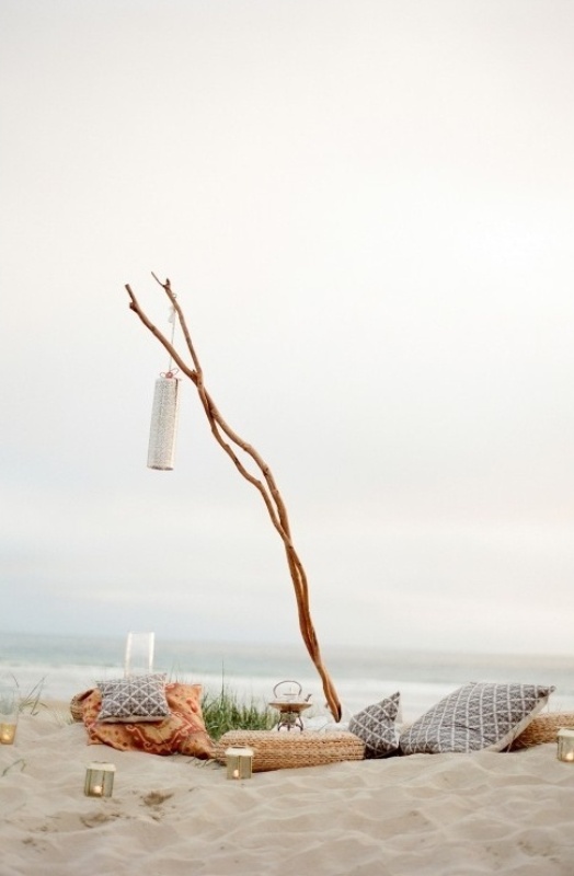 A neutral beach lounge with pillows, driftwood, candle lanterns and blankets is a great idea for a beach wedding