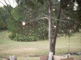 a simple outdoor wedding lounge with planked neutral furniture, white upholstery and lights over the space, hanging down from the tree