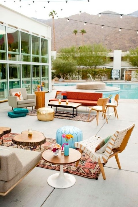 a mid century boho colorful outdoor lounge with rich stained furniture, neutral and bright upholstery and colorful pillows, rugs and poufs