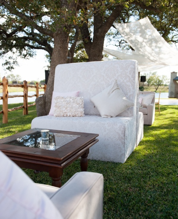 A refined outdoor wedding lounge with printed sofas, dark stained coffee tables, curtains over the chairs