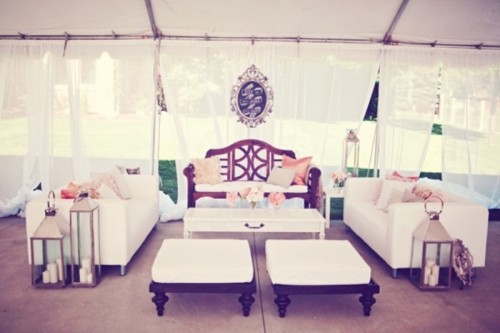 a white wedding lounge in a tent, low ottomans and low coffee tables and large lanterns and bright pillows
