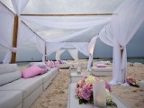 a white beach wedding lounge with neutral sofas, low coffee tables and ottomans, neutral curtains over the space