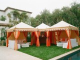an outdoor wedding lounge in tents, with white sofas and bright pillows and bold blooms on the tables