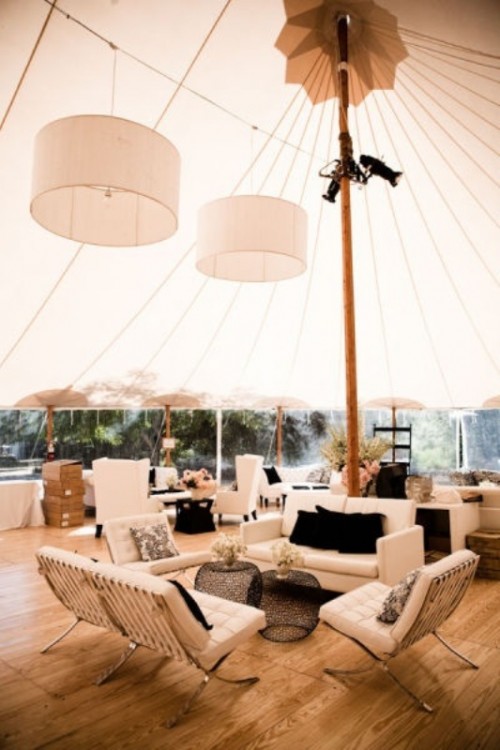 a neutral wedding lounge in a tent with modern neutral furniture, black pillows and black coffee tables, neutral blooms and pendant lamps