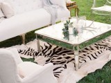 an elegant white wedding lounge with refined furniture, a low shiny coffee table, a zebra rug and some greenery and candles
