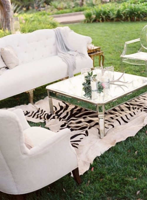 an elegant white wedding lounge with refined furniture, a low shiny coffee table, a zebra rug and some greenery and candles