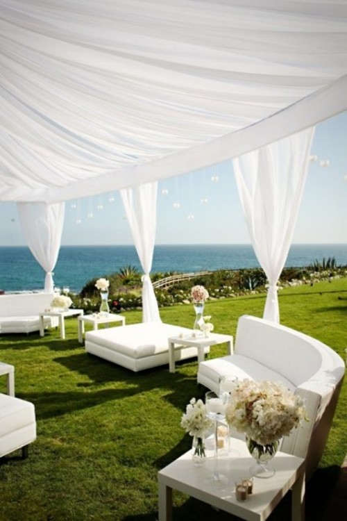 a white outdoor lounge with elegant seating furniture, white blooms and curtains and a sea view is amazing for a tropical or beach wedding
