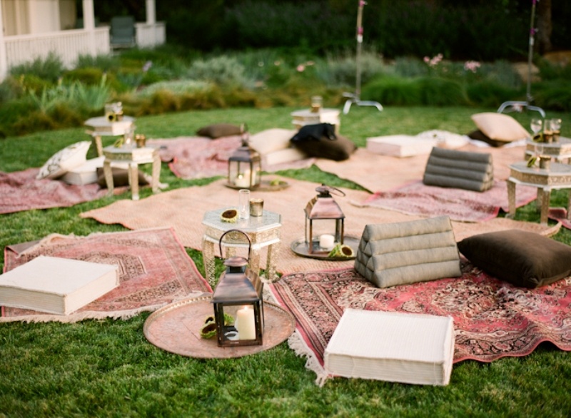 an outdoor boho pink wedding lounge with bold printed rugs, lots of pillows and cushions, candle lanterns and flowers