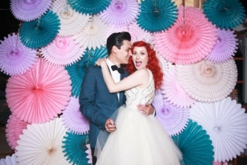 a lot of colorful paper fans on the wall are an amazing and bright wedding backdrop that cheers up the space