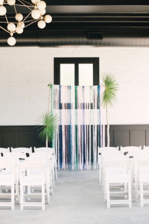 a simple wedding backdrop of colorful ribbons and some large palm leaves is a fast to DIY idea
