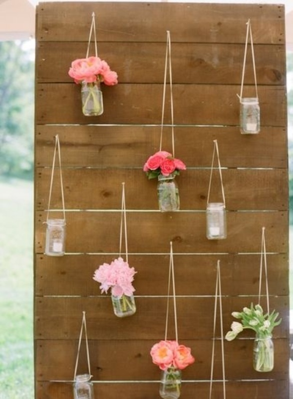 A rustic wedding backdrop with candle lanterns and bright floral arrangements in jars is a cool and cozy idea