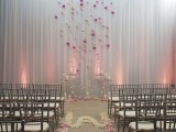 a white curtain with bright pink and neutral blooms attached, with candles on stands and on the floor plus more blooms